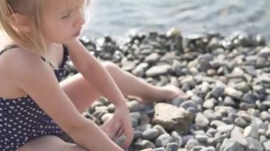 Mayolu küçük bir kız çakıl taşı kumsalında taş bir kule inşa ediyor.