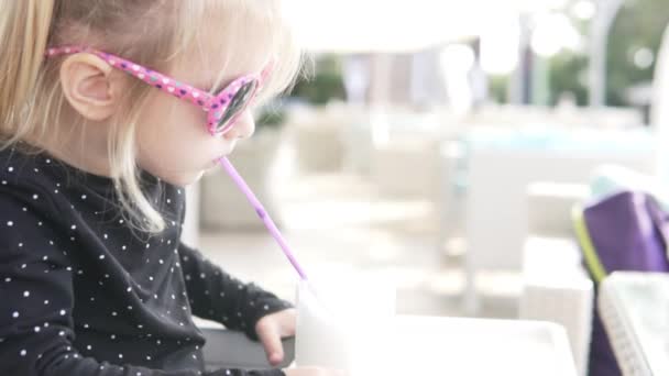 Маленькая девочка в солнечных очках пьет молочный коктейль — стоковое видео