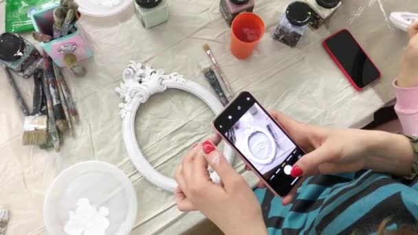 Una mujer toma un marco de fotos decorado en un teléfono en una clase magistral . — Vídeo de stock