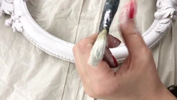 Woman examines a brush smeared with white paint in a creative lesson on painting frames — Stock Video