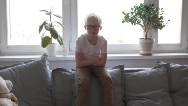 The boy sits at home on the sofa, — Stock Video