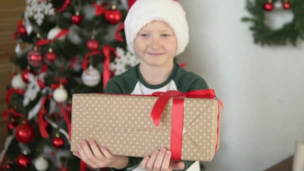 Un niño en un sombrero de Santa Claus da un hermoso regalo — Vídeos de Stock