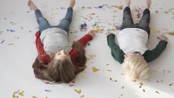 Los niños hacen ángeles de nieve en un suelo blanco con confeti . — Vídeos de Stock