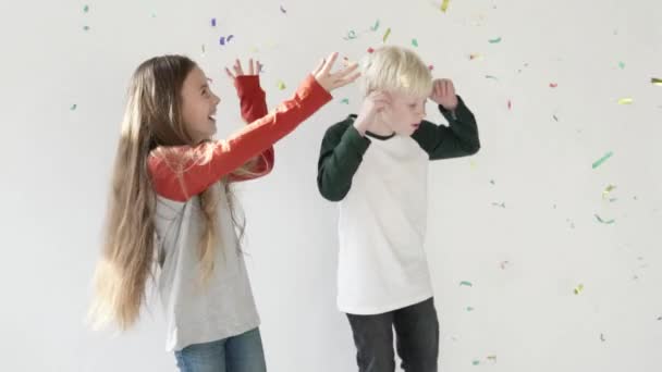 Un niño y una niña se regocijan en un saludo de confeti de papel — Vídeos de Stock