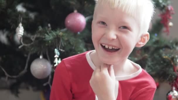 Хлопчик у новорічному костюмі Санта сміється на прикрашеній ялинці — стокове відео
