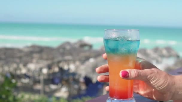 Женщина рукой берет стакан разноцветного коктейля в баре у моря — стоковое видео