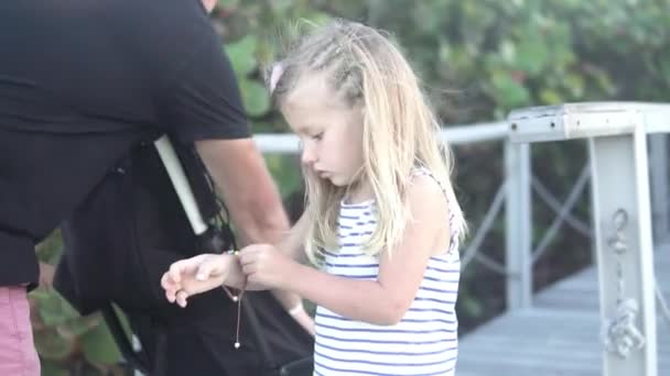 Apa egy kislány karkötőt tesz a karjára. — Stock videók