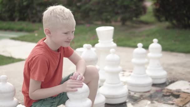 Lindo menino loiro joga xadrez grande no hotel — Vídeo de Stock