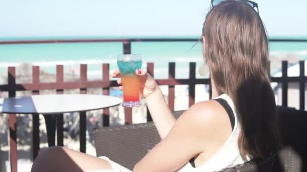 Uma mulher bebe um cocktail num bar na praia — Vídeo de Stock