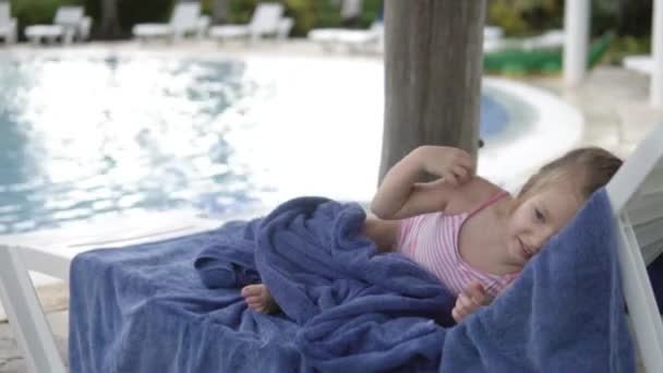 Una niñita yace en un Chaise junto a la piscina infantil — Vídeo de stock