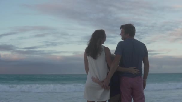 Семья стоит обнимаясь на пляже и смотрит на океан — стоковое видео
