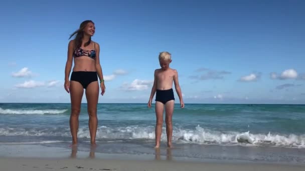 母と息子は陽気に海のそばのビーチにジャンプします — ストック動画