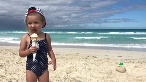 Маленькая девочка в купальнике ест мороженое на пляже — стоковое видео
