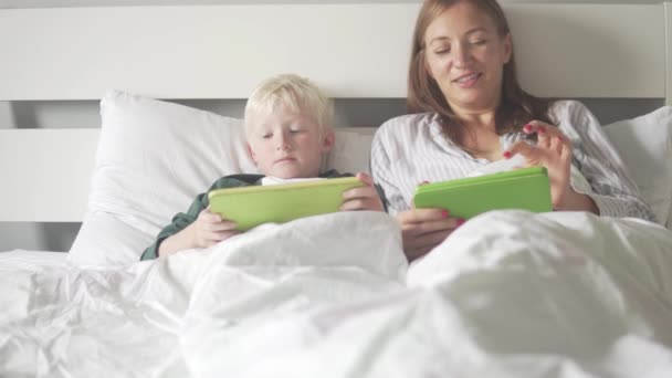 Mamá e hijo se acuestan en la cama por la mañana y comprueban las redes sociales en tabletas — Vídeo de stock