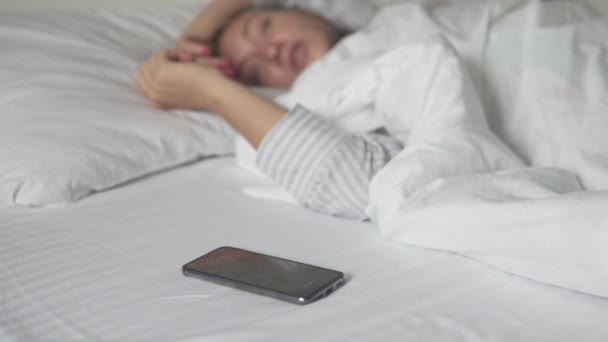 A woman turns off the alarm on her phone in the morning in the bed. In the focus of the phone — Stock Video