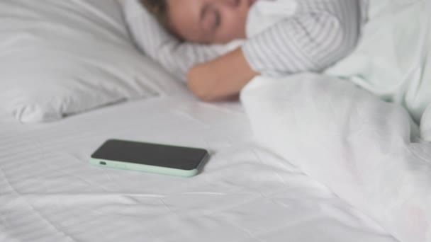 Una joven duerme en una cama junto a su teléfono móvil — Vídeo de stock