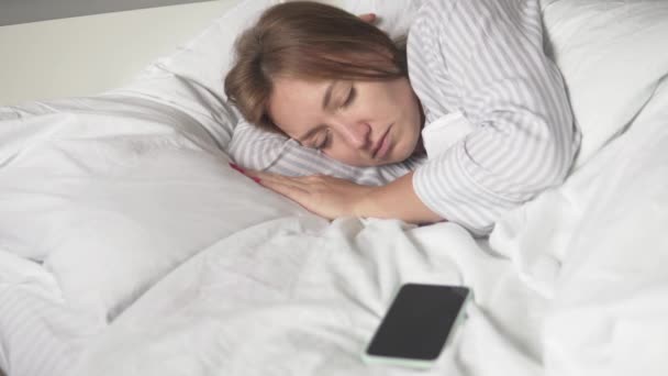 Una mujer duerme en una cama por la mañana, suena su teléfono móvil — Vídeos de Stock