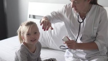 Kadın bir doktor, çocuğun vücut ısısını elektronik termometreyle ölçer..