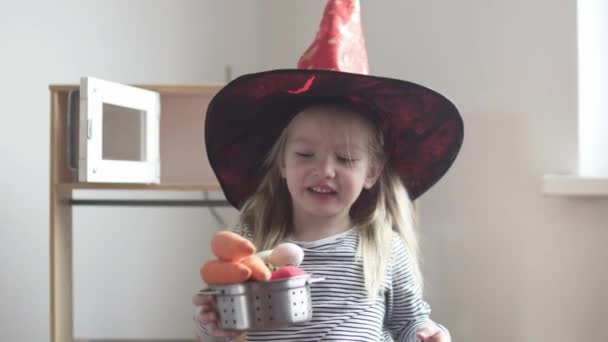 Grappig klein meisje strekt een pan met speelgoed groenten in de camera — Stockvideo