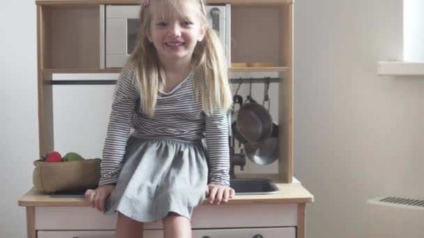 La niña se sienta en la cocina de juguete, riendo — Vídeo de stock