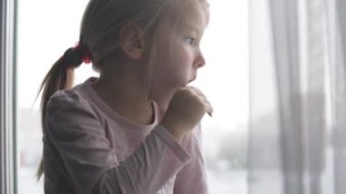 Küçük bir kız ilk kar yağdığında pencereden dışarı bakar.