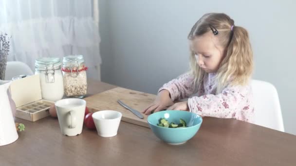 Uma menina coloca pepinos picados em um prato de salada — Vídeo de Stock