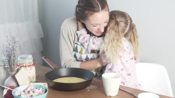 Маленька дочка ніжно обіймає матір за кухонним столом — стокове відео