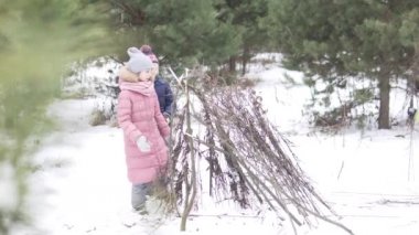 Çocuklar kışın ormanda kuru dallardan bir kulübede dururlar.