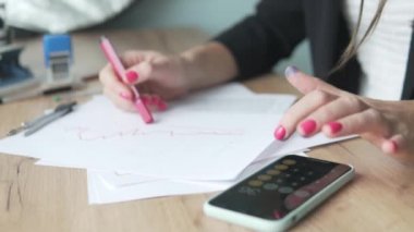 Ofisteki kadın kağıtlarla çalışıyor ve hesap makinesindeki verileri sayıyor.