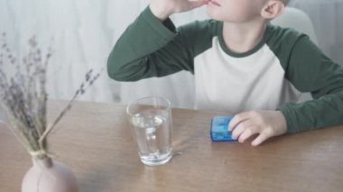 Çocuk albino ilaç yiyor ve onu evde, masada suyla yıkıyor.