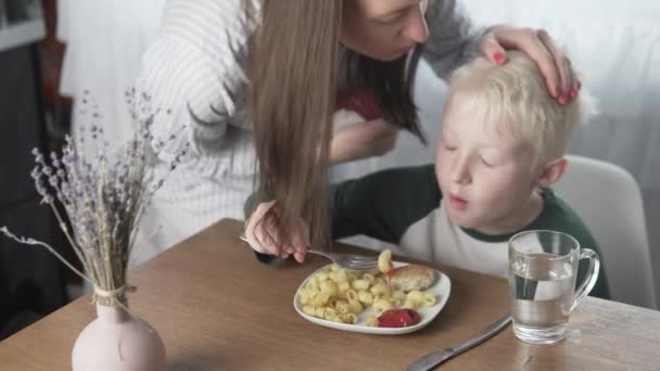Мама наливает кетчуп на тарелку своих сыновей макаронами и фрикадельками за обедом — стоковое видео