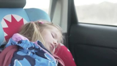 A beautiful little girl sleeps in a car in a car seat