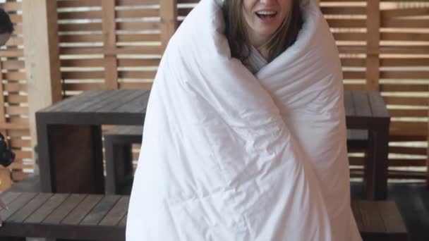 Een mooie vrouw in een deken staat 's morgens op de veranda van het huis — Stockvideo