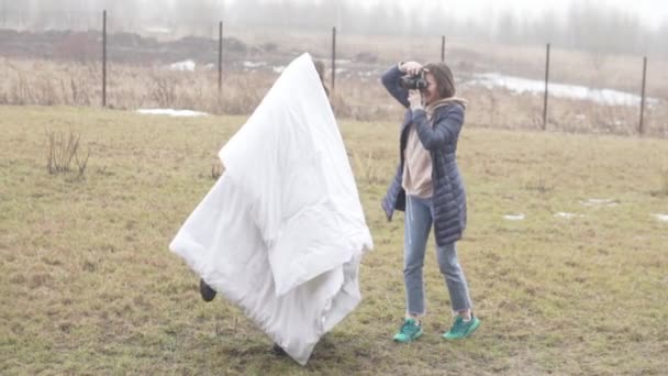 Uma fotógrafa está fotografando um modelo em um cobertor fora — Vídeo de Stock