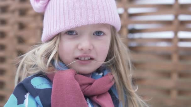 Una bella bambina con un cappello rosa su una passeggiata lancia una palla di neve — Video Stock