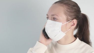 Telefonda tıbbi maske takan bir kadın var.
