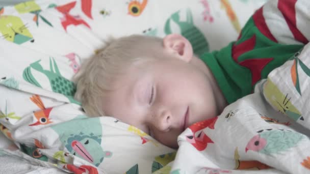 Ένα ξανθό αγόρι ξυπνάει στο κρεβάτι το πρωί. — Αρχείο Βίντεο
