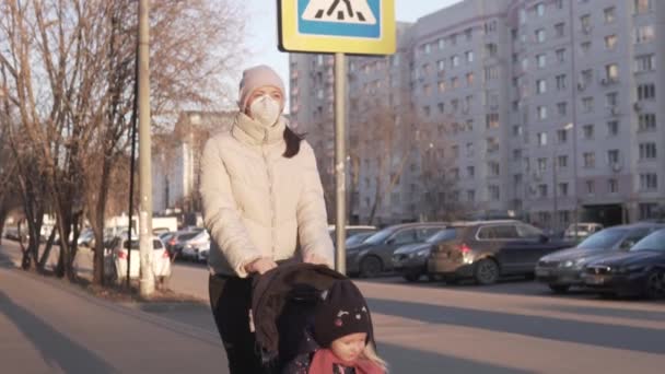 Una mujer con una máscara médica camina con un niño en un cochecito — Vídeos de Stock