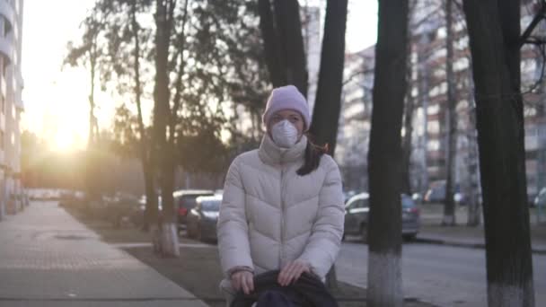 Uma mulher mascarada caminha com uma criança em um carrinho na rua ao pôr do sol . — Vídeo de Stock