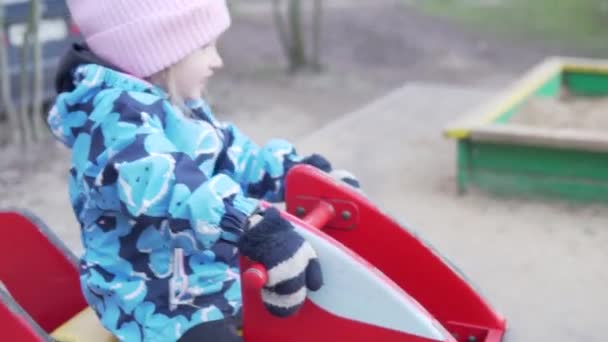 Маленькая девочка катается на качелях на детской площадке весной — стоковое видео
