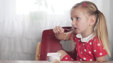 Küçük bir kız evde, mutfakta süzme peynir yiyor.