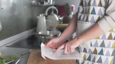 Kadın çorba tarifini okuyor ve kaynar suya sarı mercimek döküyor.