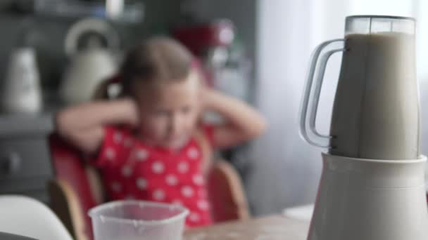 Een klein meisje plugt haar oren uit het geluid van een werkende blender in de keuken. — Stockvideo