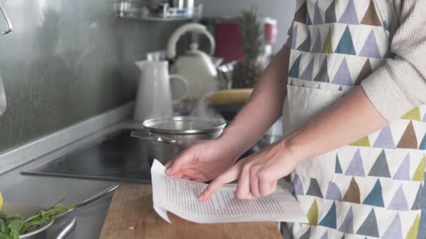 La mujer lee la receta de sopa y vierte lentejas amarillas en agua hirviendo — Vídeo de stock