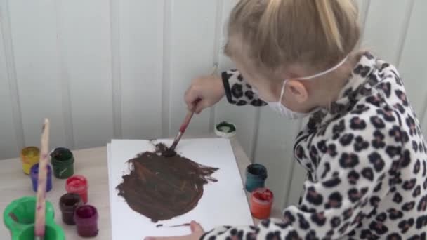 En liten flicka i en medicinsk mask i ansiktet målar. — Stockvideo