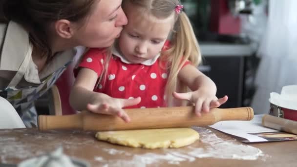 Una niña enrolla la masa con un rodillo en casa en la cocina . — Vídeo de stock