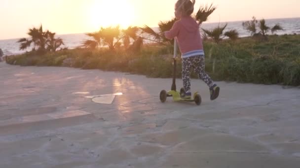 Uma menina monta uma scooter ao longo do mar à noite — Vídeo de Stock