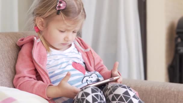 En liten flicka tittar på en tecknad film på en mobiltelefon under karantänen av huset på balkongen — Stockvideo