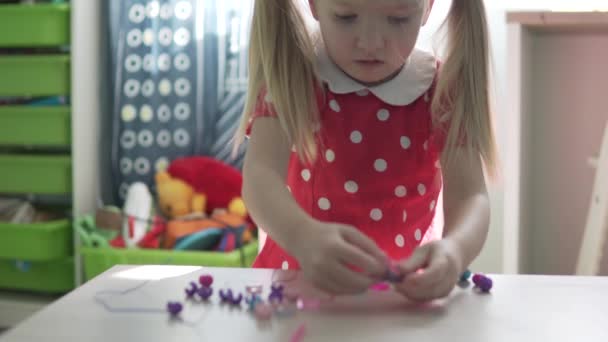 Seorang gadis kecil membuat gelang dari manik-manik di rumah — Stok Video