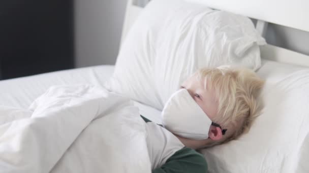 Nemocný chlapec v ochranné masce leží doma v posteli. — Stock video